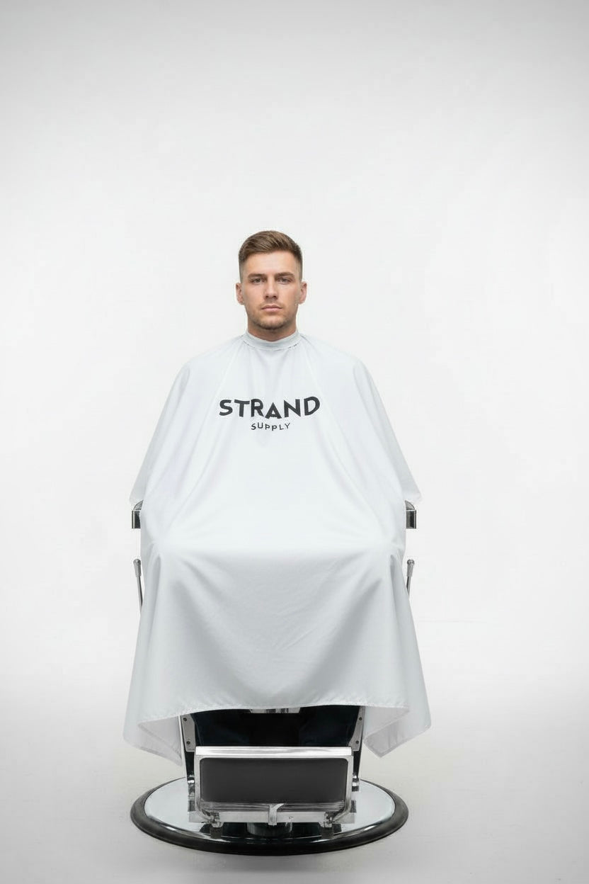 Person wearing a white barber cape with 'Strand Supply' branding on a white background