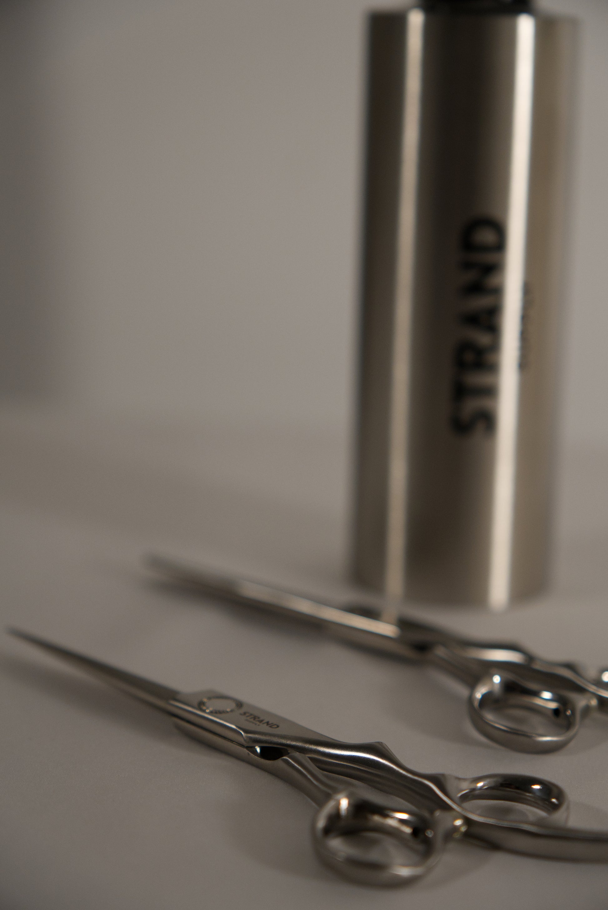 Metallic scissors and a cylindrical container labeled 'Strand' on a neutral background